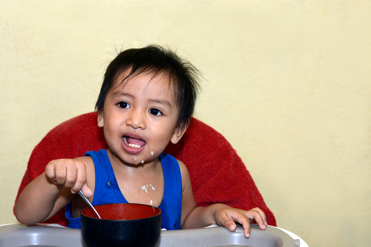 1 year old baby boy learning to eat alone smiling
